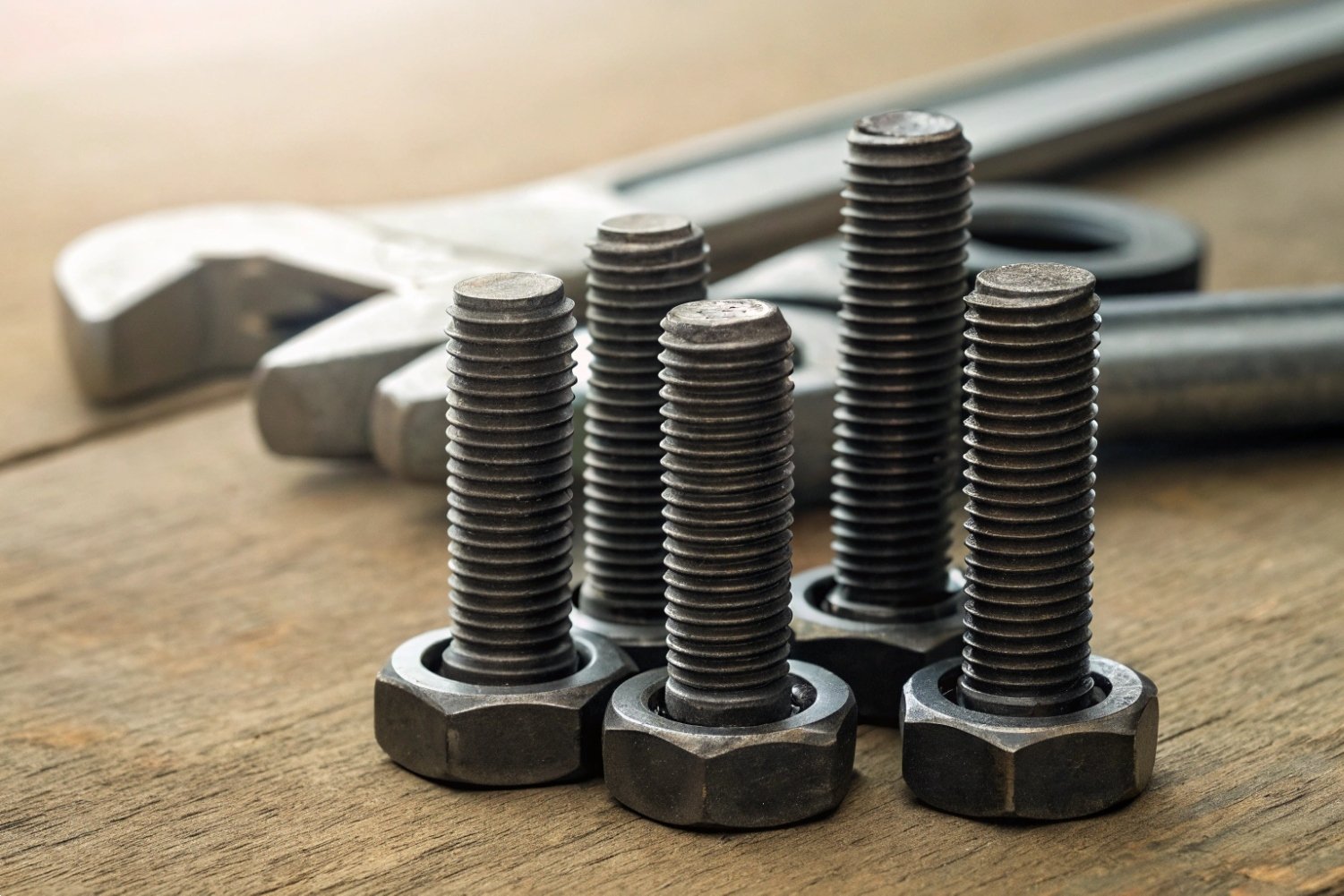 Industrial Steel Fasteners Close-up of industrial steel bolts and nuts on a rustic wooden workbench with tools.